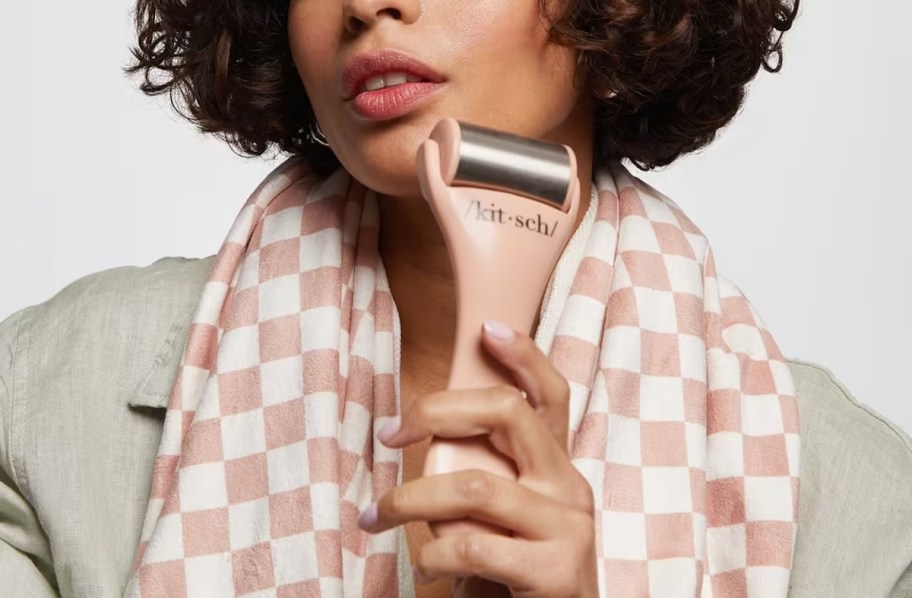 woman using kitsch ice roller on face wearing pink and white checked scarf