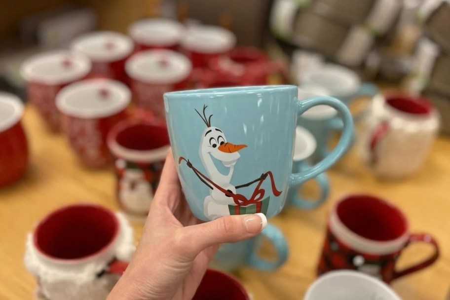 a womans hand holding a kohls olaf holiday mug