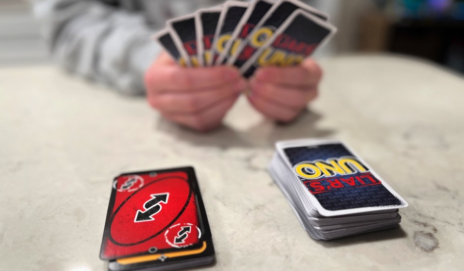person holding cards from a liar's uno card game behind two stacks of cards