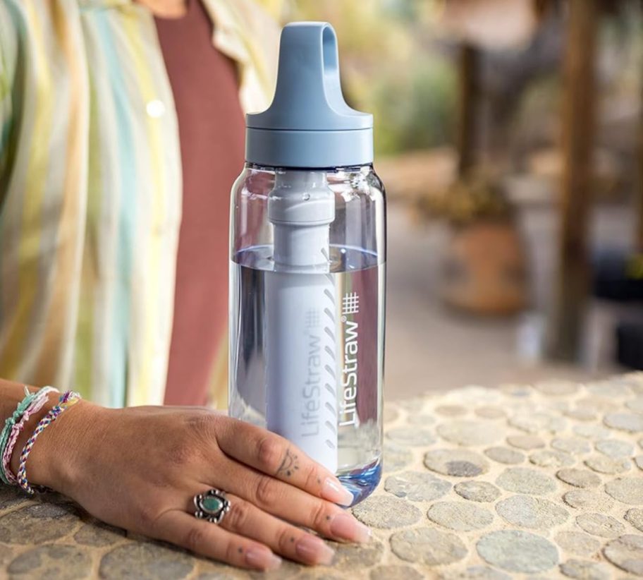 Hand holding a life straw water bottle on Stone pebble counter
