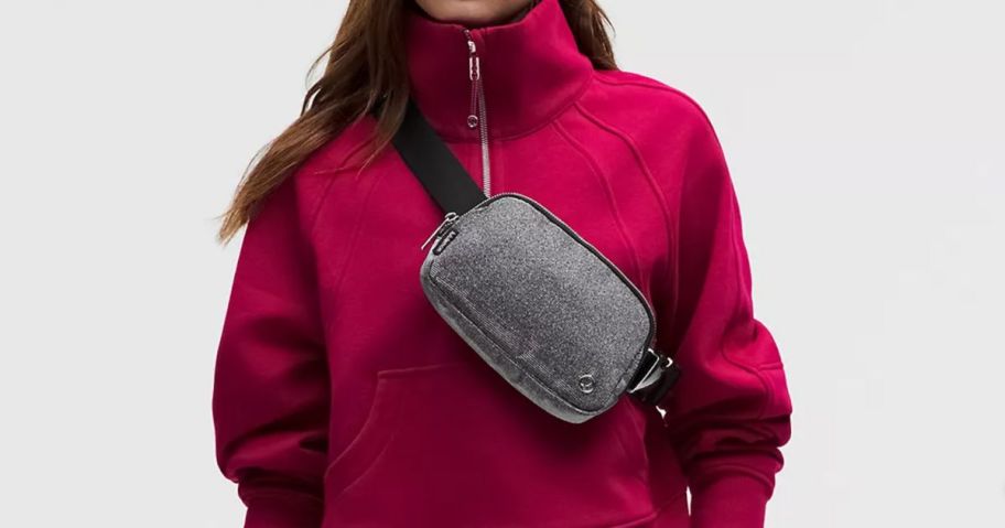 A person wearing a pink sweatshirt with a glittery belt bag across their chest