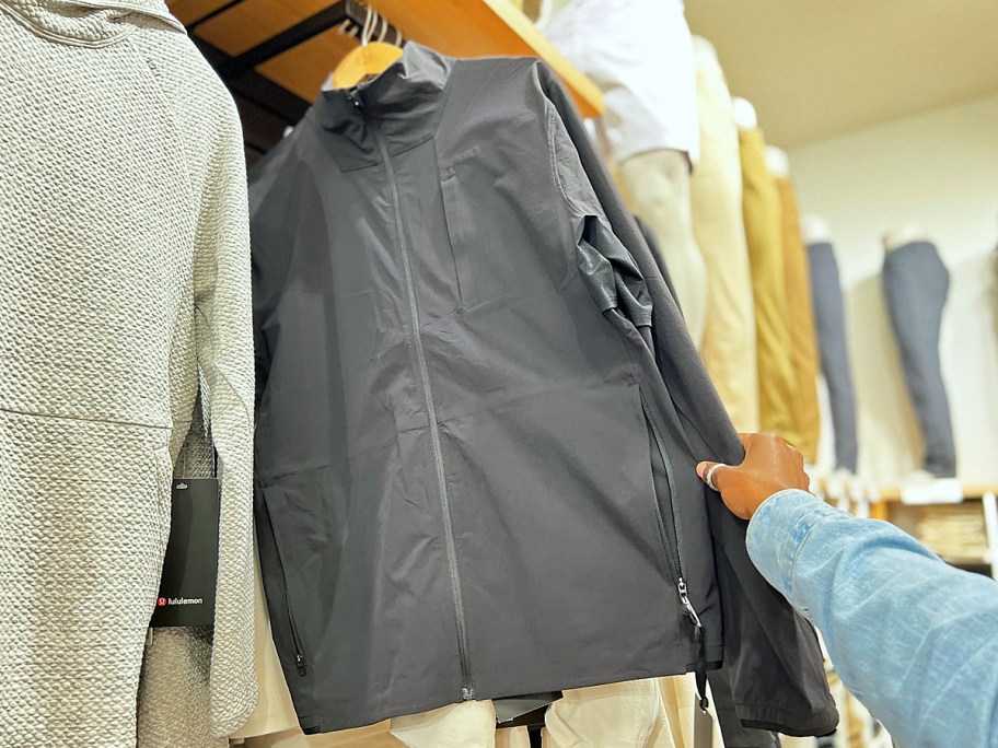 hand grabbing a black rain jacket from store rack