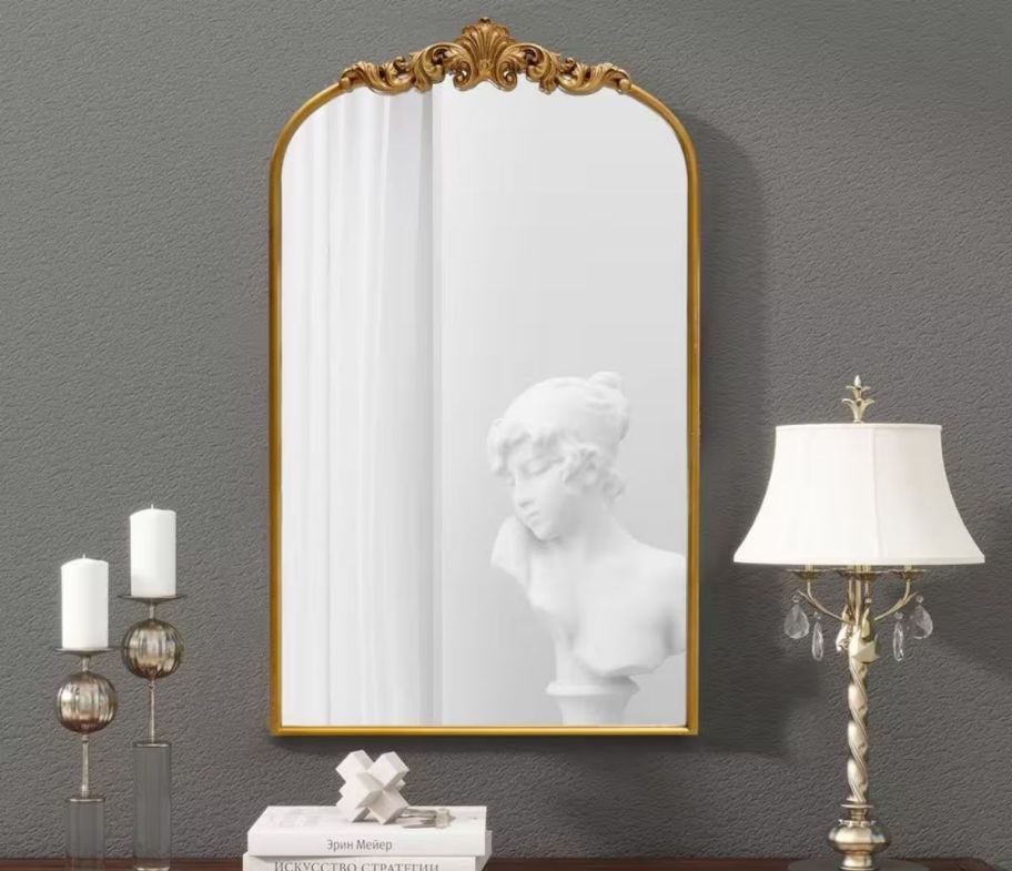 arched gold wall mirror hanging above a console table