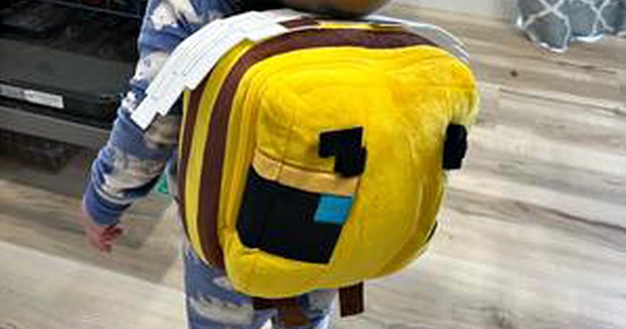 Child wearing a plush, pixelated-style yellow backpack with blue and black accents, reminiscent of a Minecraft bee.