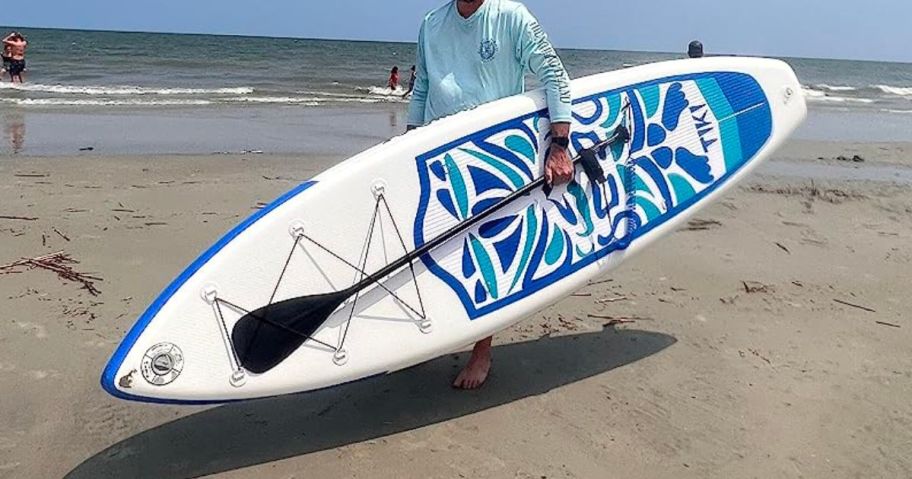 man holding paddleboard on beach
