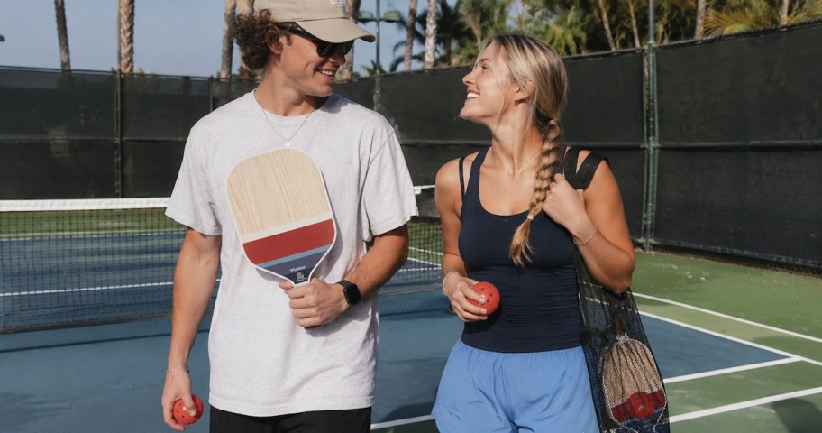 teen guy and gurl walking on court outside holding pickleball set