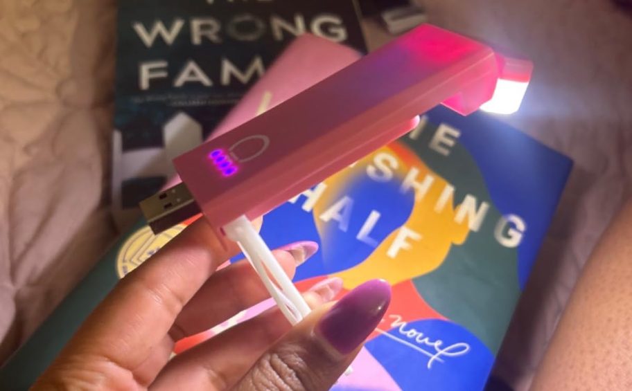 hand holding pink book light lit up in front of pile of books