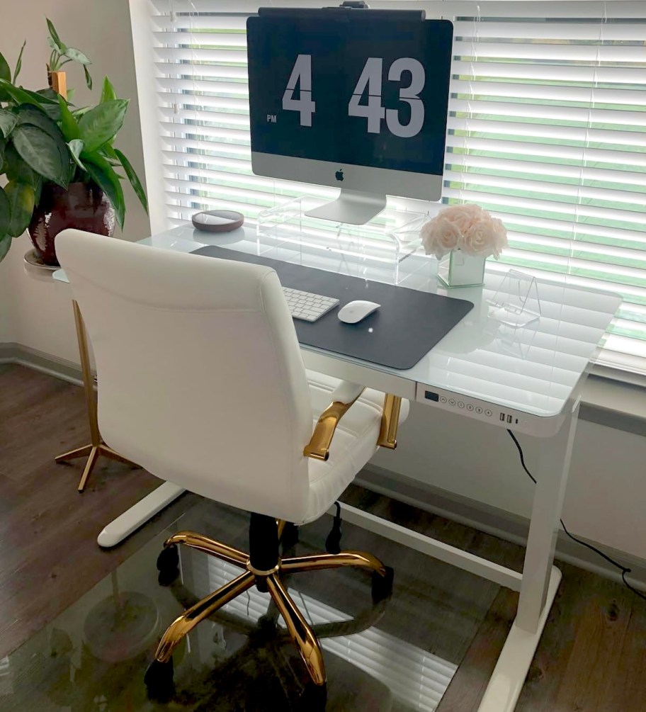 white glass top desk with computer and chair in front of window