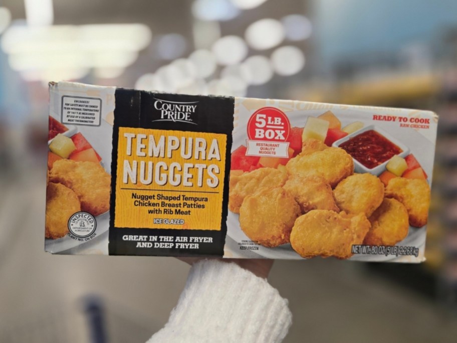 a womans hand holding a box of tempura chicken nuggets