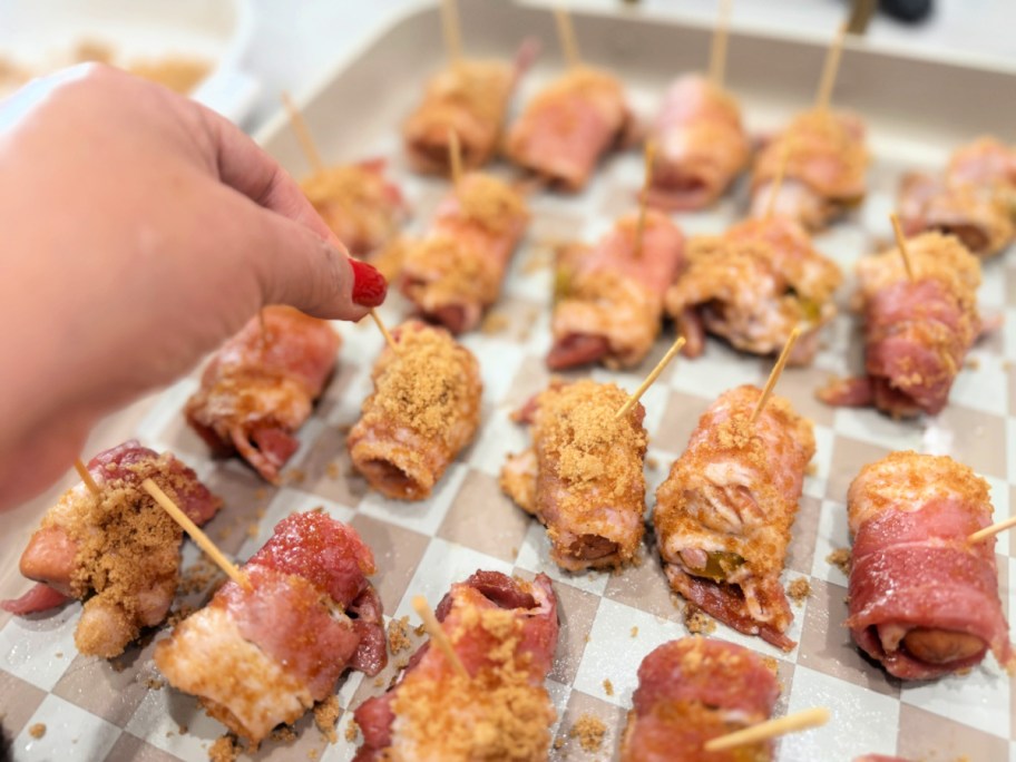 using a toothpick to wrap bacon around lil smokie sausage 