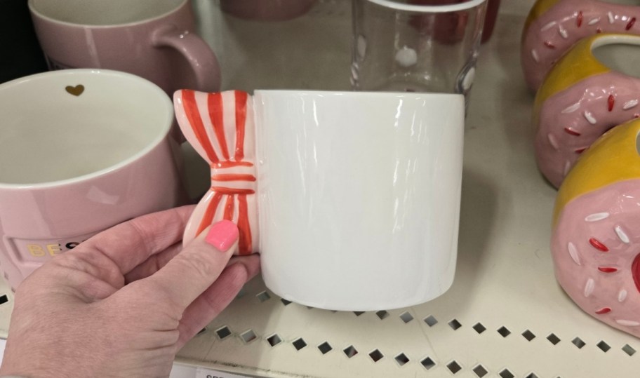 womans hand holding a red white and pink bow coffee mug