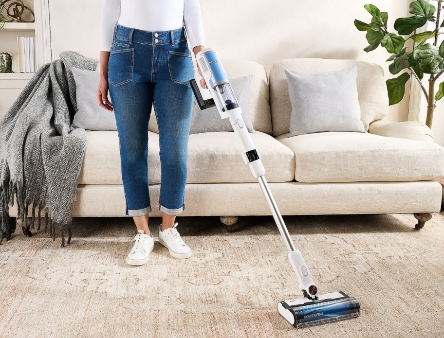 a woman using a stick vac to clean a rug