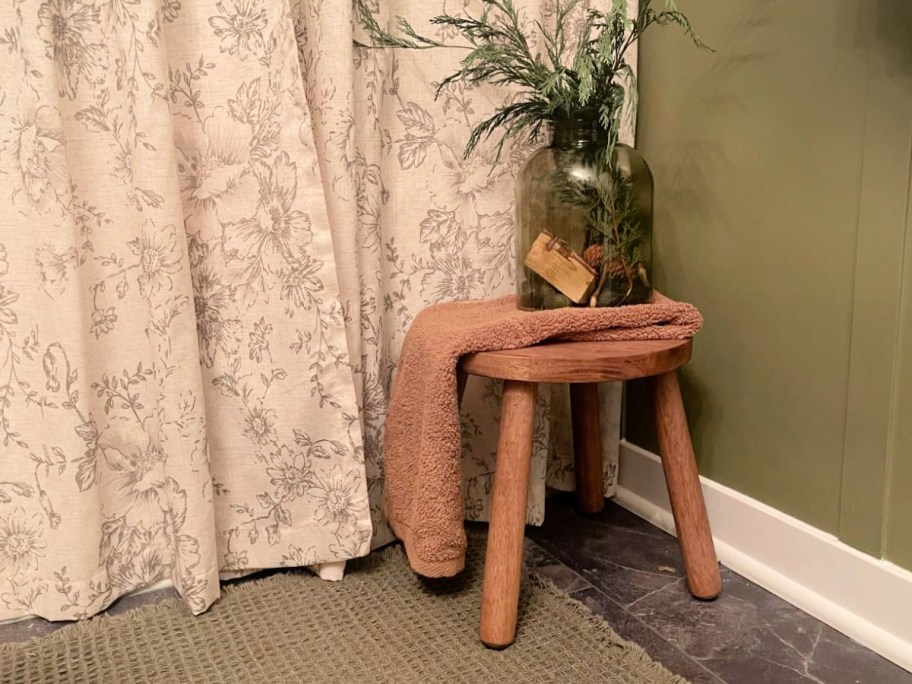 wooden plant stool next to floral curtain
