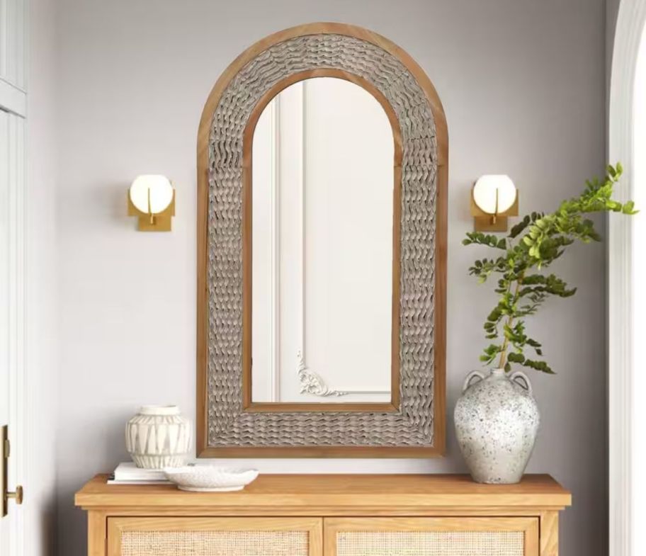 arched wooden wall mirror hanging above a console table