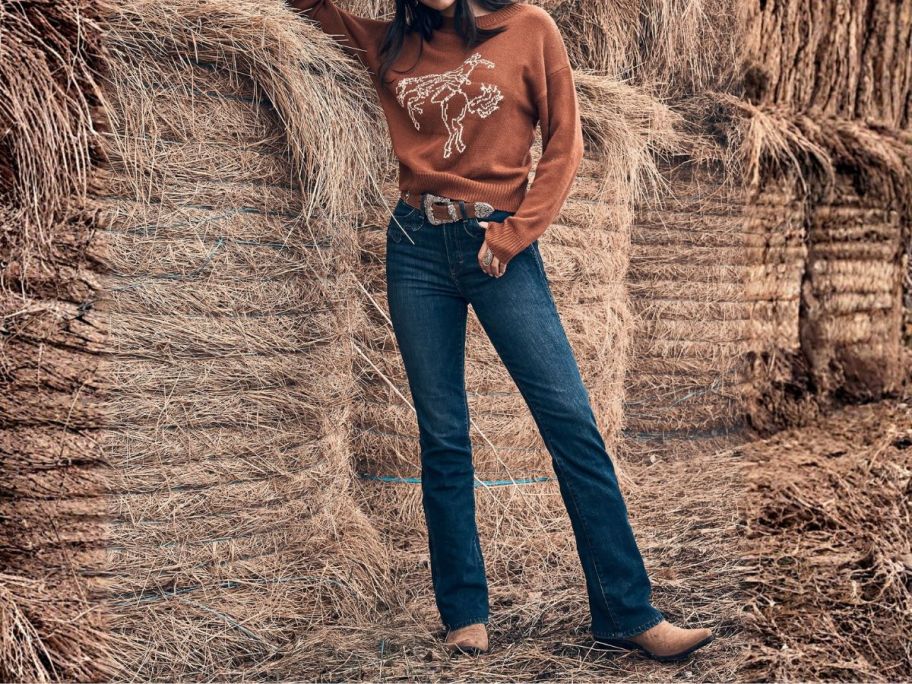 woman wearing wrangler jeans leaning against haystack