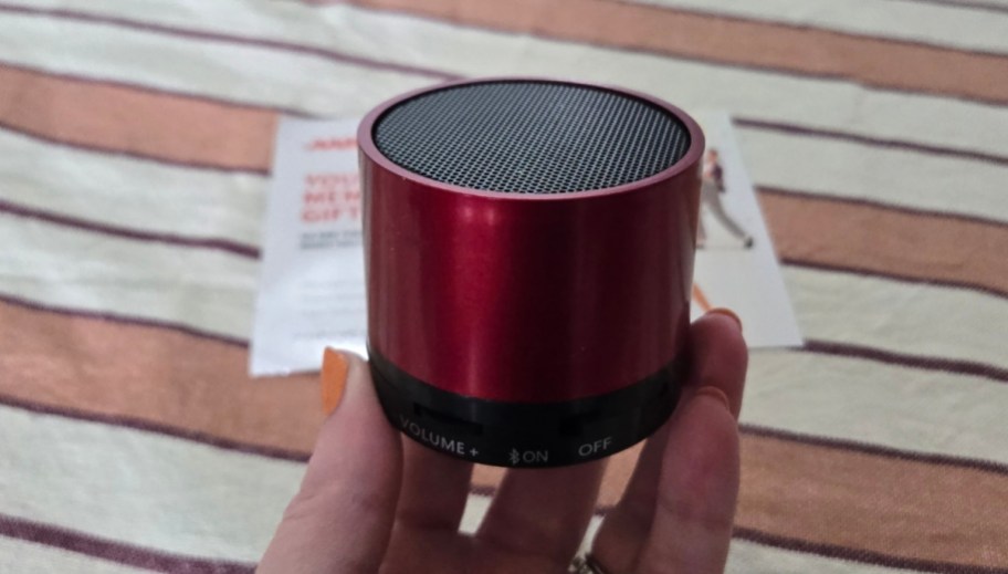 a womans hand holding a red bluetooth mini speaker