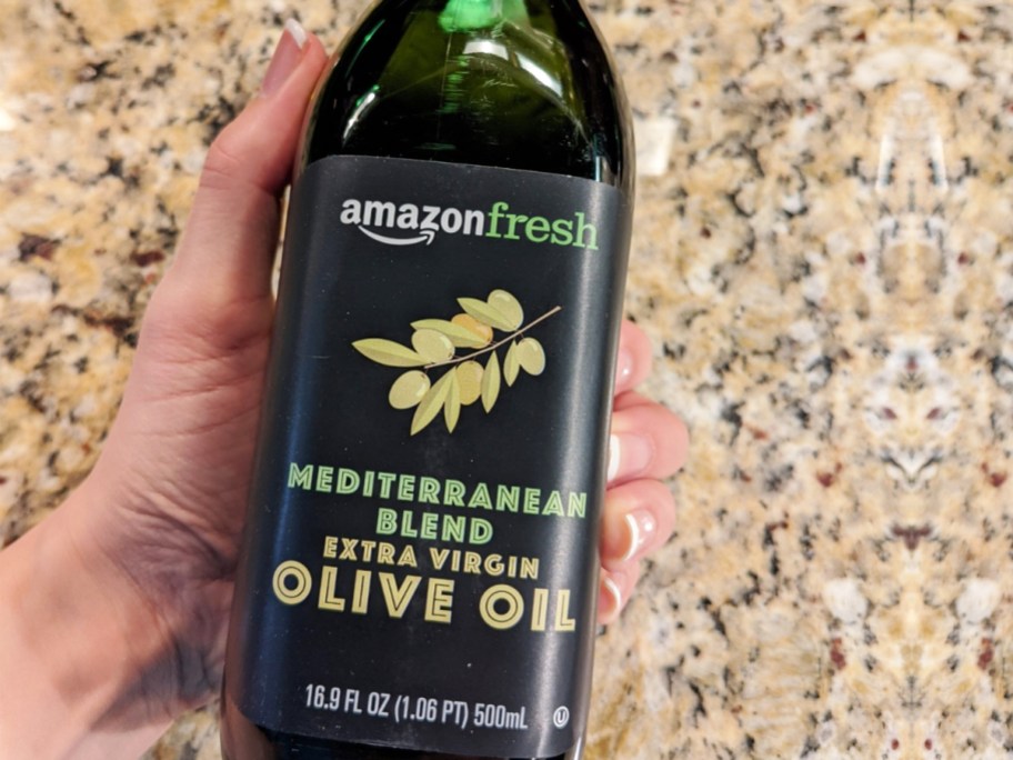 hand holding a bottle of Amazon Fresh Mediterranean Extra Virgin Olive Oil