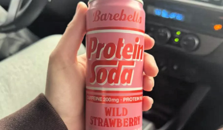 Person holding can of barbells protein soda, while sitting in car