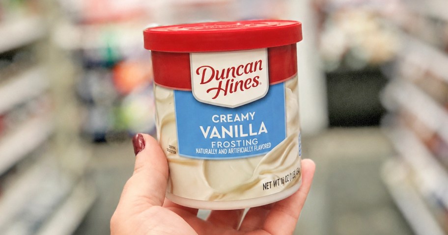hand holding up a can of Duncan Hines Creamy Vanilla Frosting in store aisle