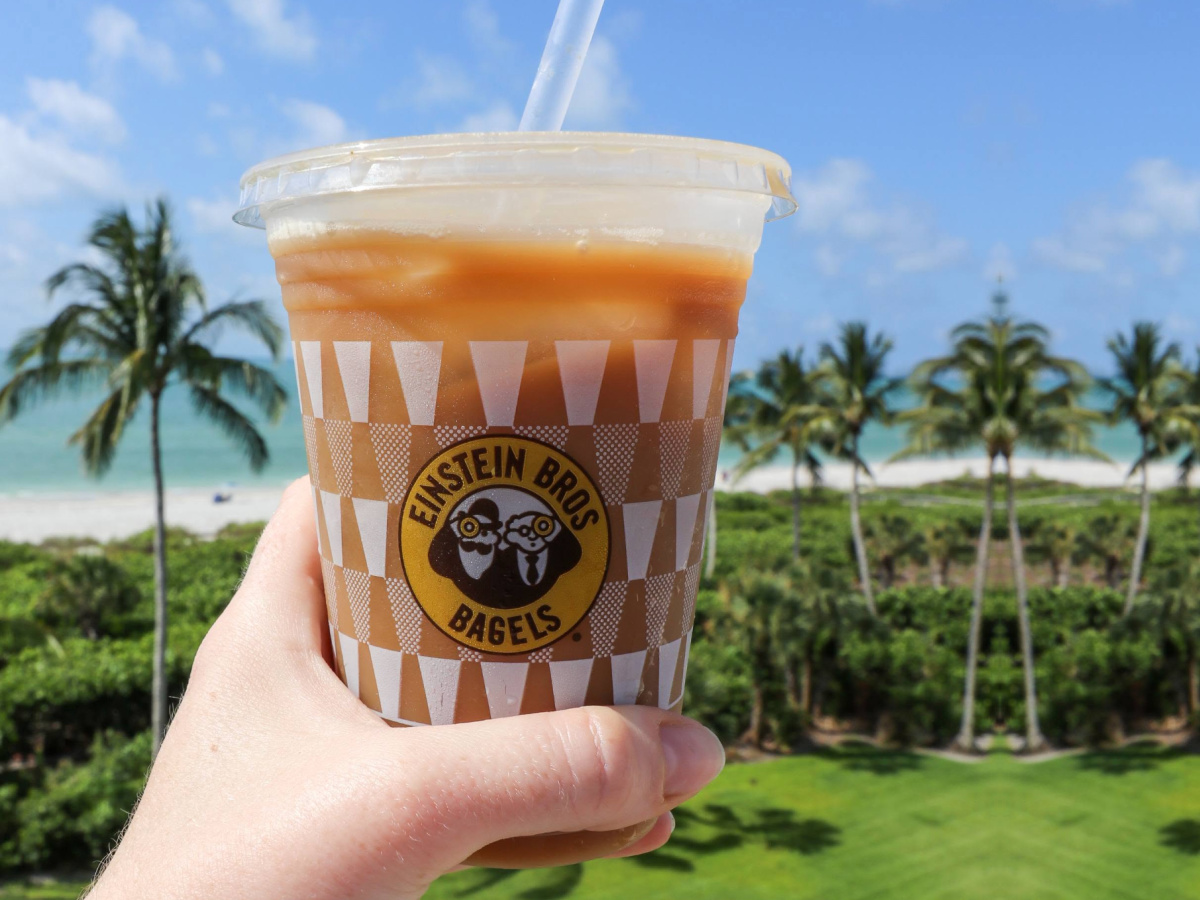 Hand holding Einstein Brothers iced coffee with beach in the background