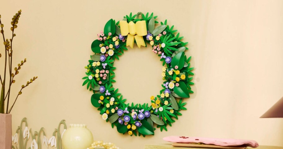a LEGO Spring wreath with LEGO flowers and a yellow bow hanging on a wall