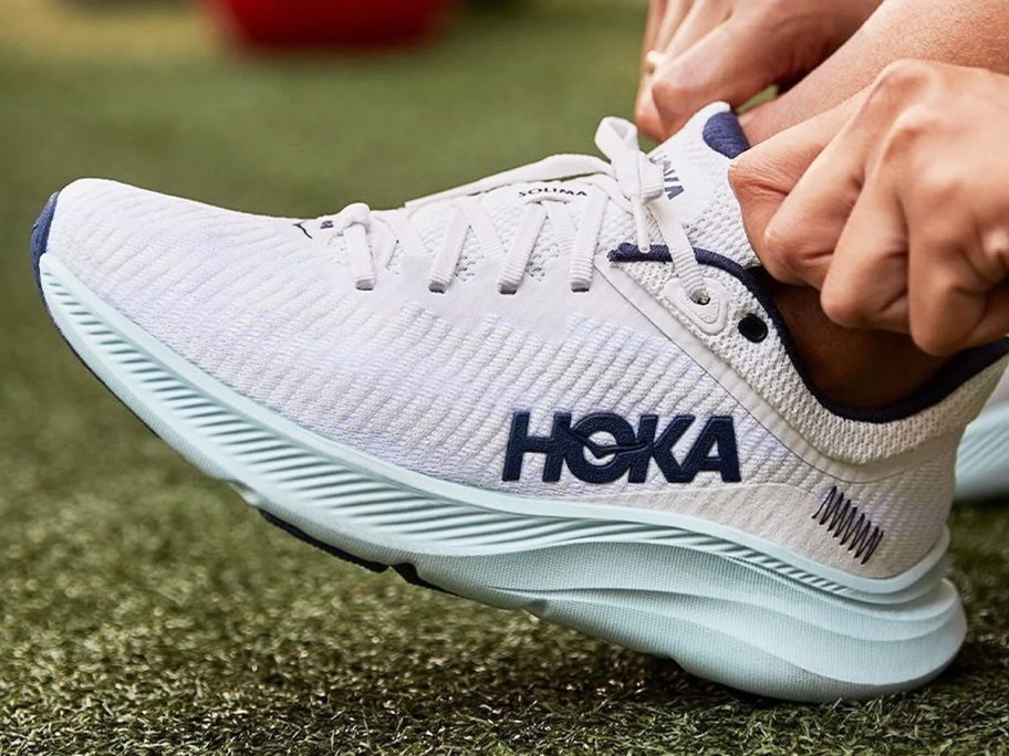woman putting a white hoka running shoe on her foot