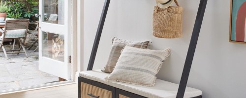 Black Hall Tree with bench drawers. It's in an entryway with a bag and hat hanging on it.
