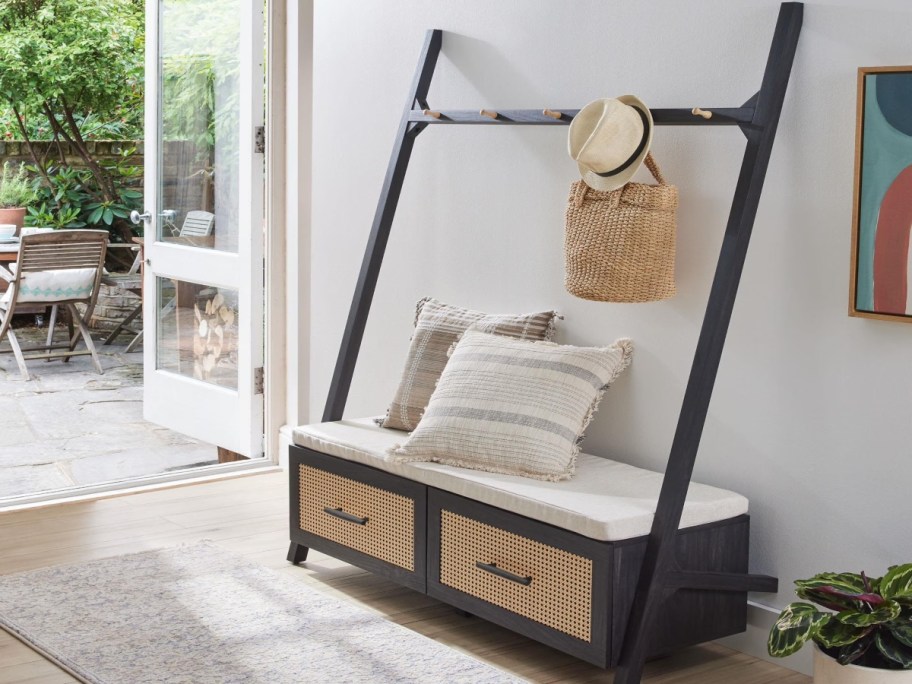 Black Hall Tree with bench drawers. It's in an entryway with a bag and hat hanging on it.