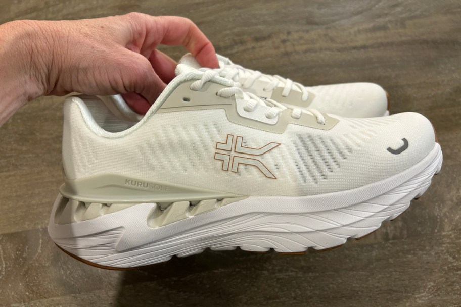 hand grabbing pair of cream sneakers