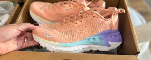 hand grabbing peach orange sneaker out of box