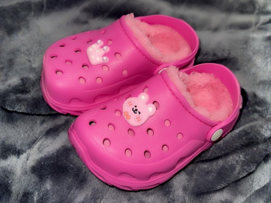 pair of pink sherpa-lined clogs on fleece blanket