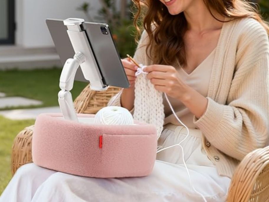 A woman crocheting with a fluffy tablet stand