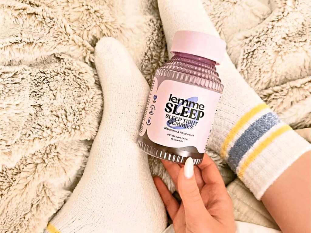 Woman holding bottle of sleep gummies while sitting on blanket and wearing socks