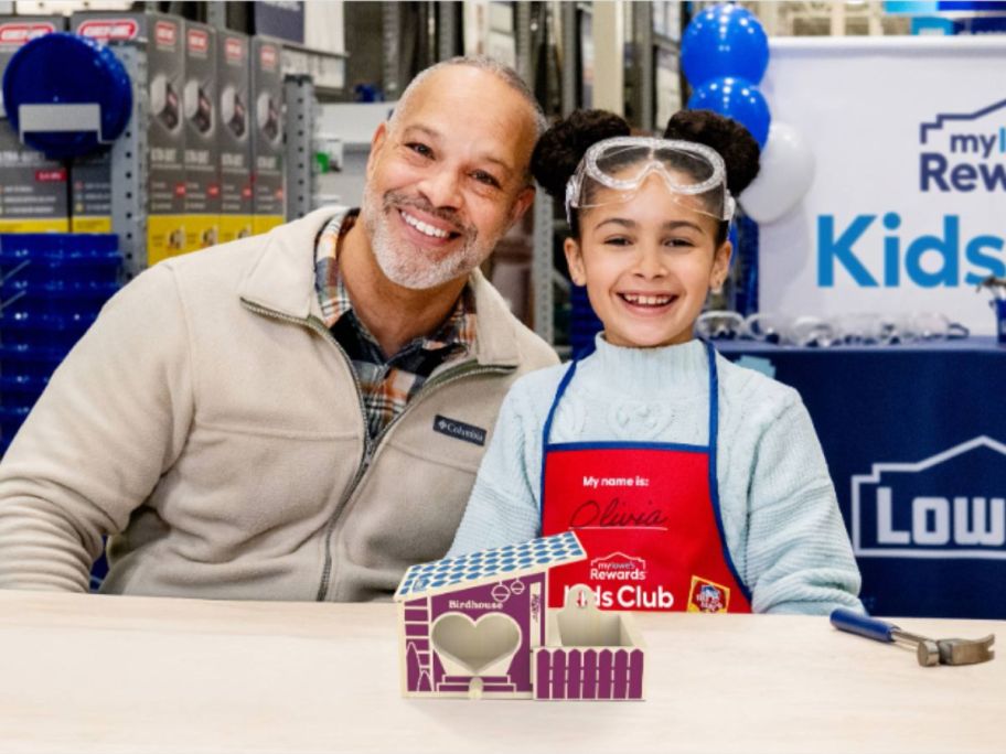 A man and a child posing in back of a small wooden birdhouse at Lowe's