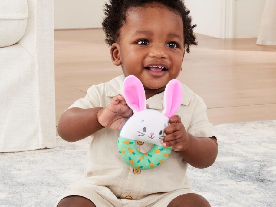 A baby holding a Ms. Rachel sensory bunny ring toy.