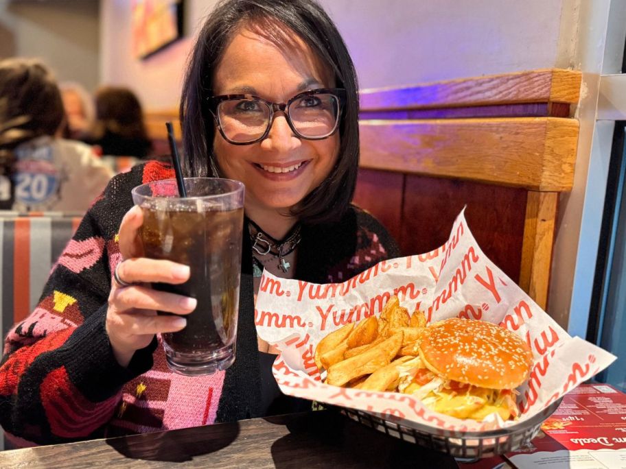 woman holding up a soda and red robin burger with fries