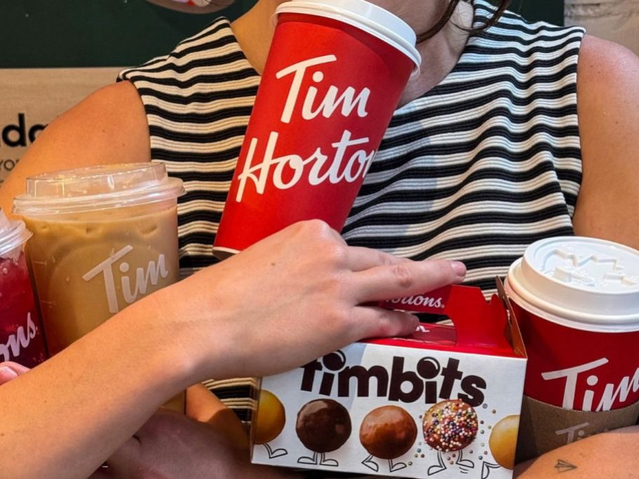 woman holding several Tim Horton's drinks and a small box of Timbits