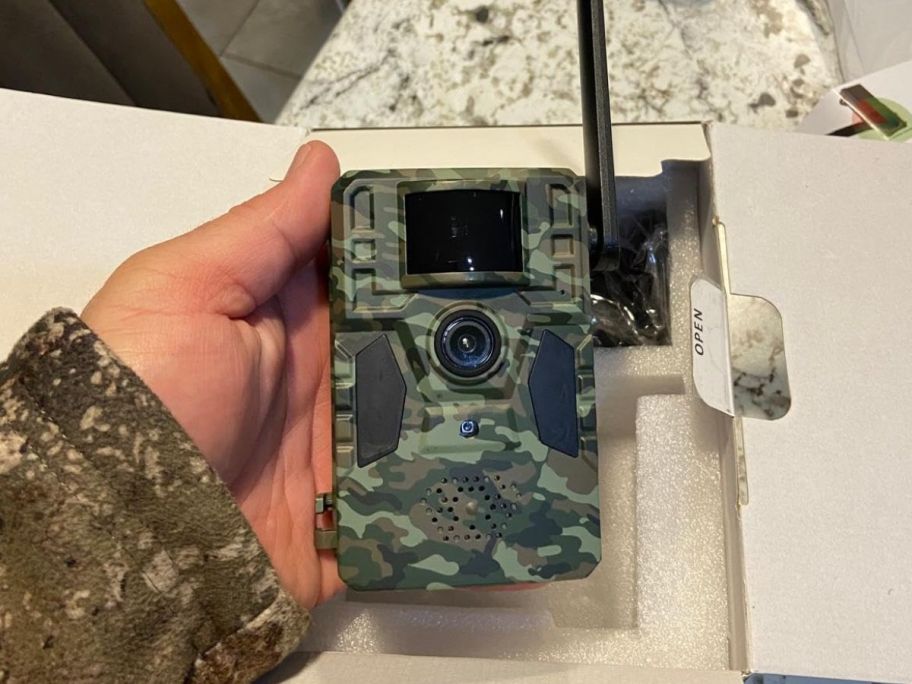 A hand holding a A trail camera in camo