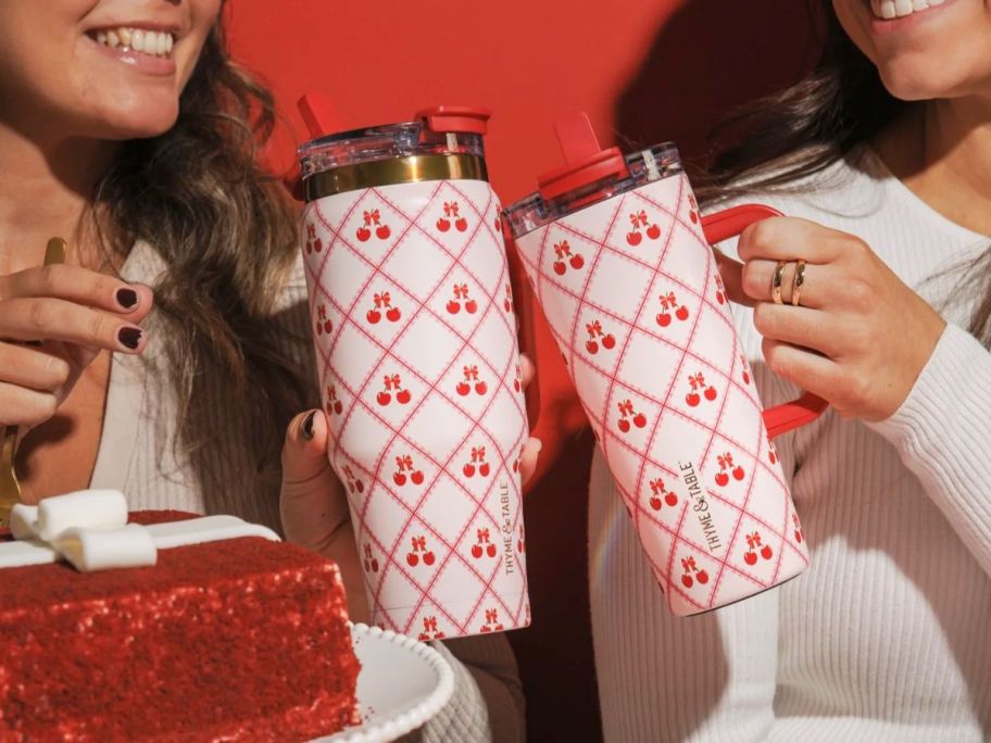 two women clinking their cherry themed tumblers together surrounded by treats