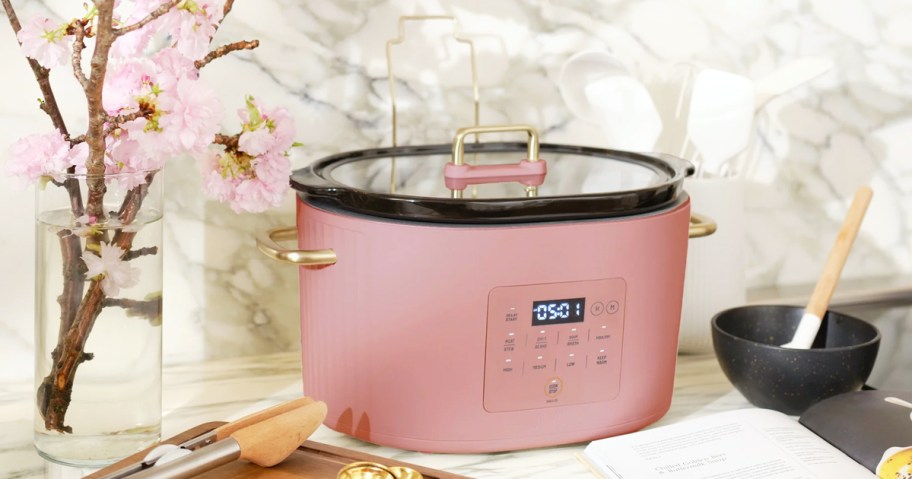 pink slow cooker on kitchen counter near pink flowers