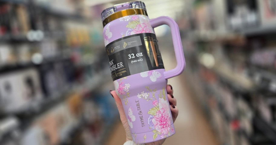 A hand holding up a purple floral tumbler.