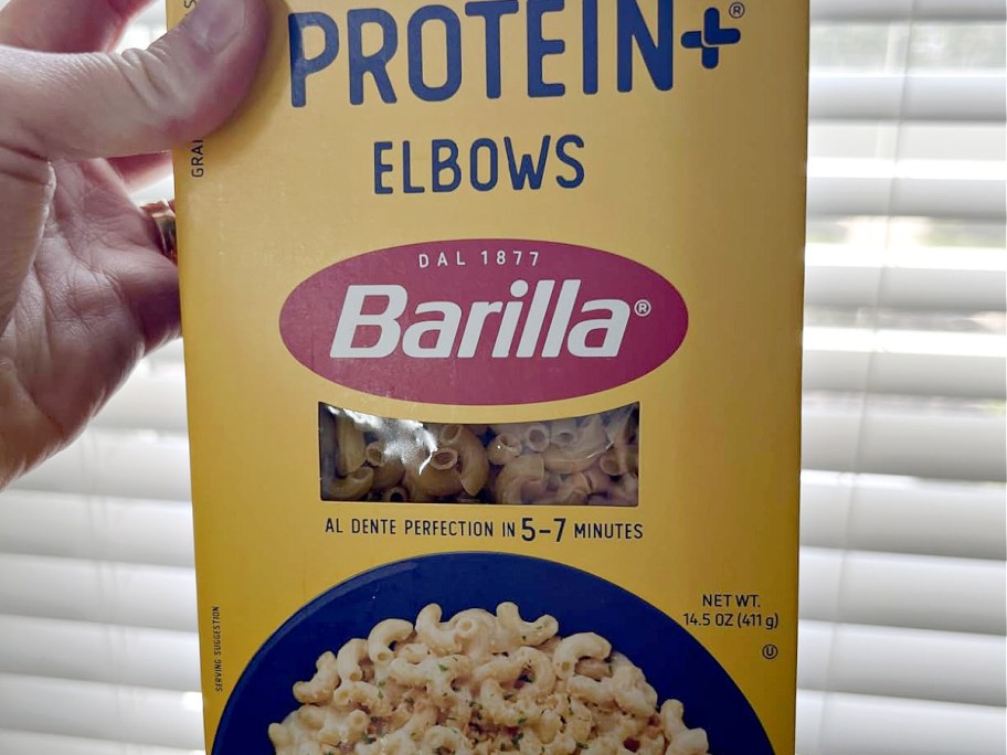 A hand holding up a box of Barilla protein pasta.