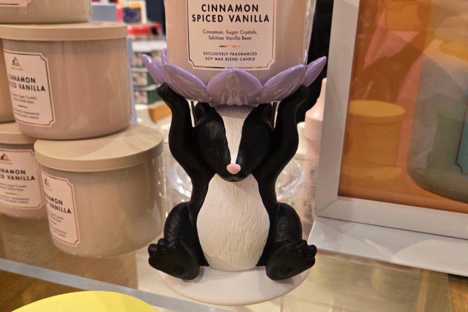 skunk holding purple flower candle holder