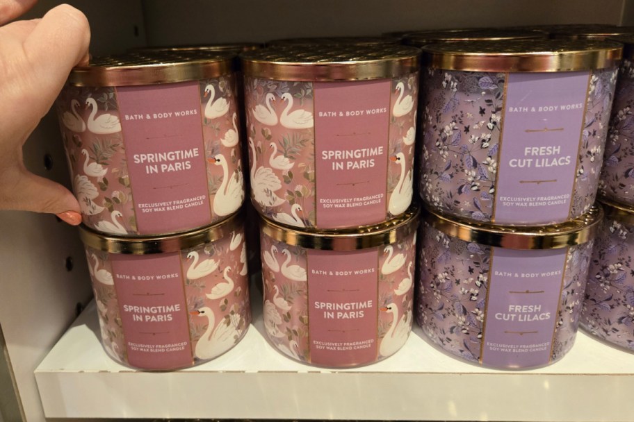 hand grabbing pink candle next to purple one on shelf