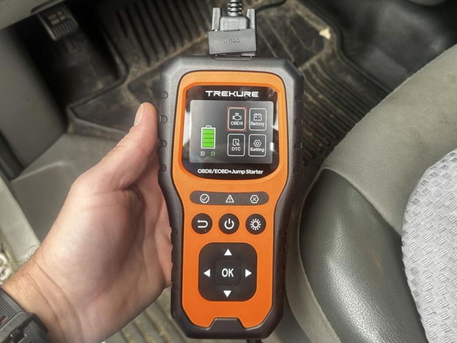 hand holding battery jumper while being used in his car