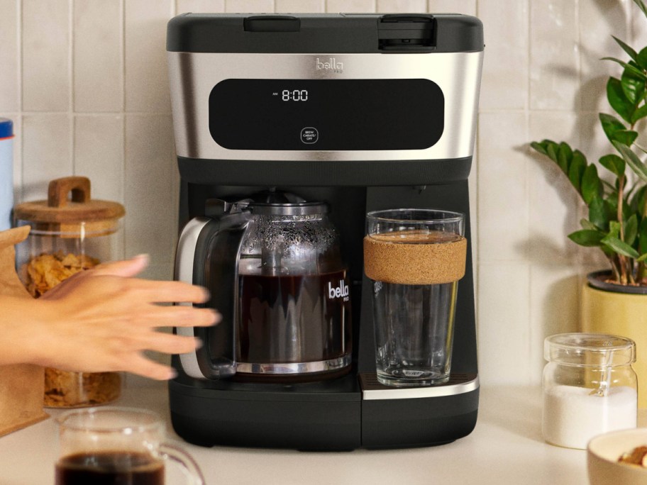 A hand reaching for the pitcher on a 12-cup coffee maker.