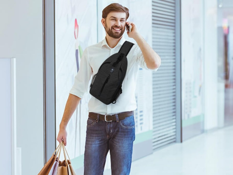 A man wearing a black crossbody bag and talking on the phone.