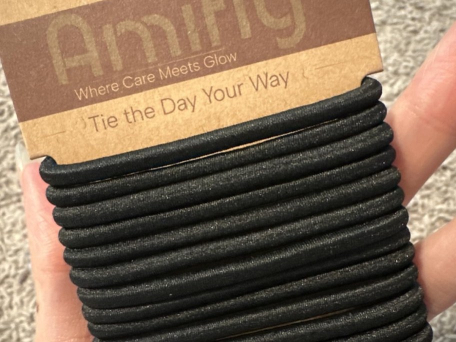A hand holding up a pack of black hair ties.