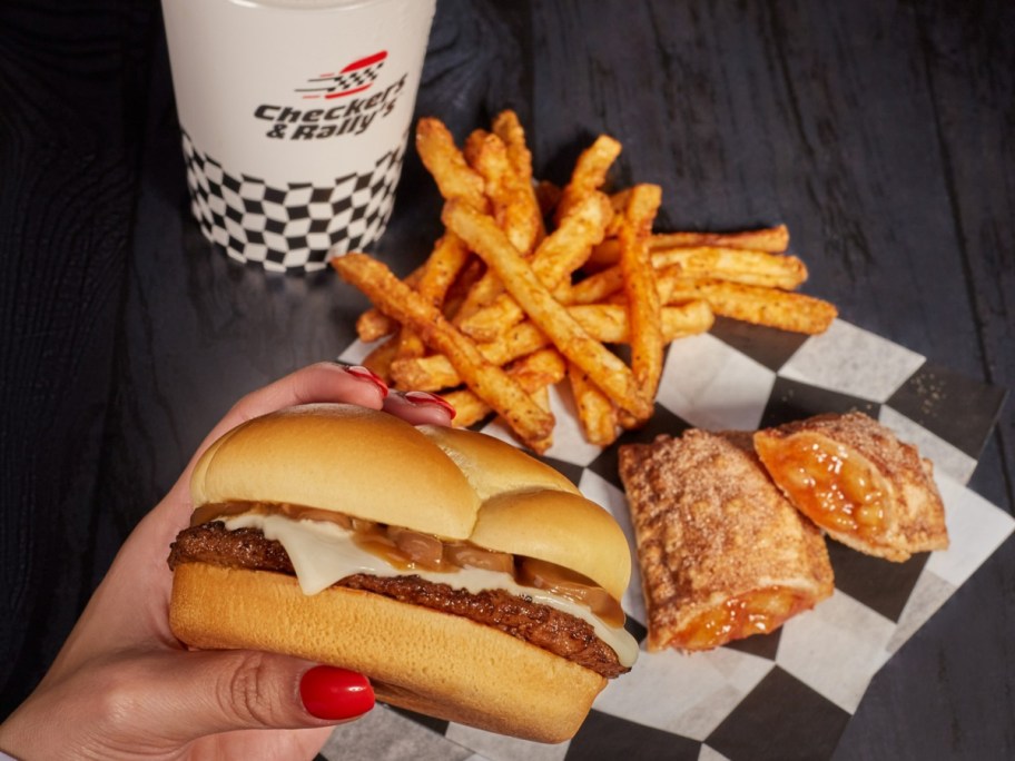 woman holding a burger next to fries, and apple pie, and a fountain drink