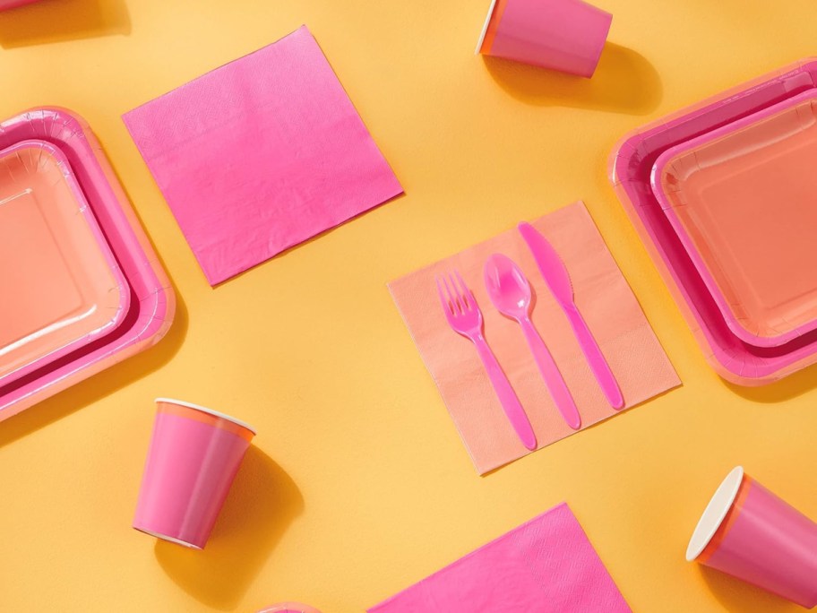 Pink and orange party supplies against a yellow background.